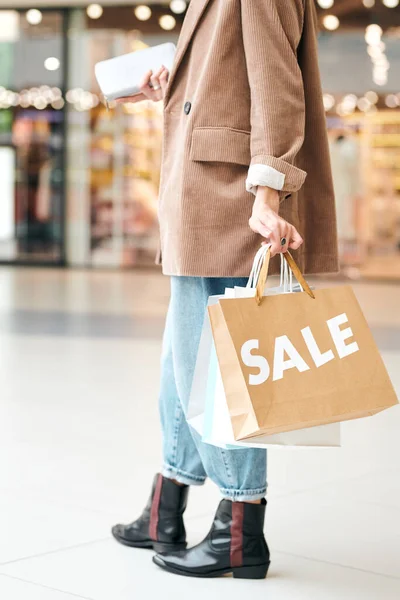 モールで大販売を楽しみながら ショッピングバッグで歩く長いジャケット姿の無名の女性のクローズアップ — ストック写真