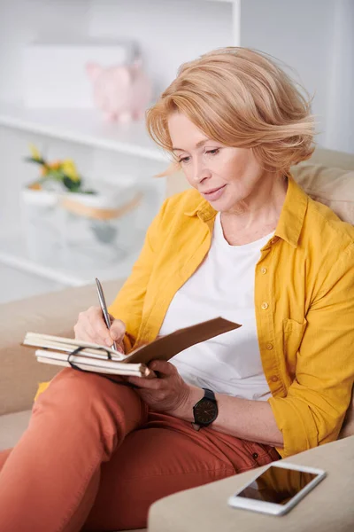Mature Blond Female Making Notes Notepad While Sitting Couch Work — Stock Photo, Image