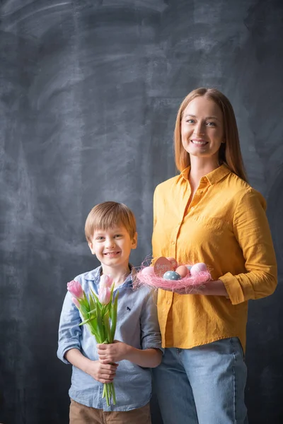 Portrait of cheerful family with Easter nest and bunch of tulips posing against blackboard