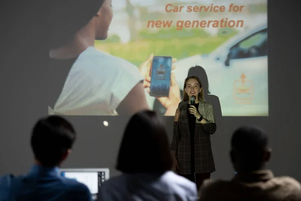 여자가 투자자들 앞에서 자동차 서비스에 아이디어를 발표하면서 마이크로 말하는 — 스톡 사진