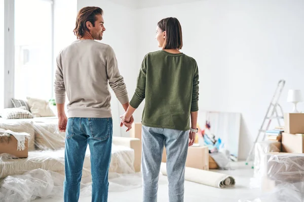 リビングルームに立ちながら手で握っている若い愛情深い夫と妻の背面図 — ストック写真
