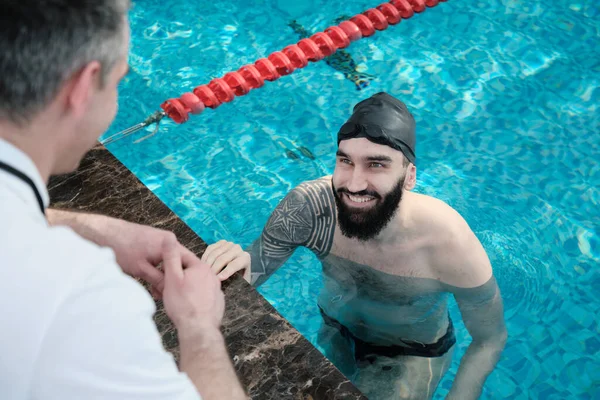 笑顔ひげを生やした水泳ともに入れ墨座ってプールとコーチに耳を傾ける — ストック写真