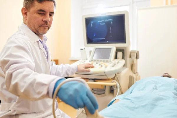 病院の患者に超音波手術をしながら プローブを使用して研究室のコートで深刻な成熟した医師 — ストック写真
