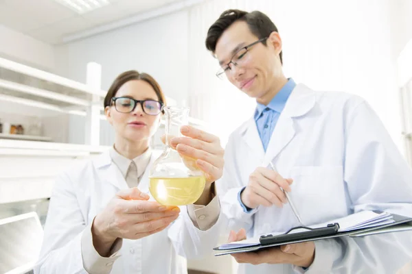 Joven Investigadora Sosteniendo Pico Con Líquido Amarillo Mientras Muestra Colega — Foto de Stock