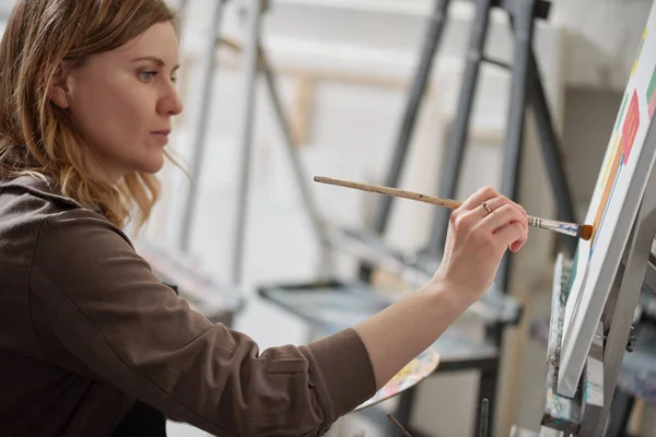 Young Serious Woman Paintbrush Looking Unfinished Picture While Sitting Front — Stock Photo, Image
