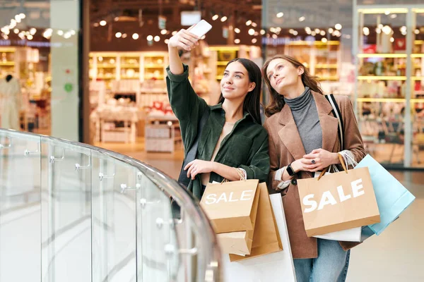 迷人的黑发女郎穿着天鹅绒衬衫 提着购物袋 和朋友在商场拍照 — 图库照片