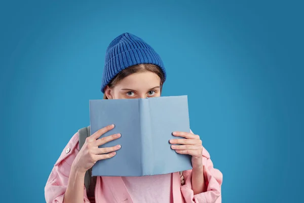 Nieśmiała Nastolatka Niebieskiej Czapce Różowej Kurtce Jeansowej Podglądająca Otwartej Książki — Zdjęcie stockowe
