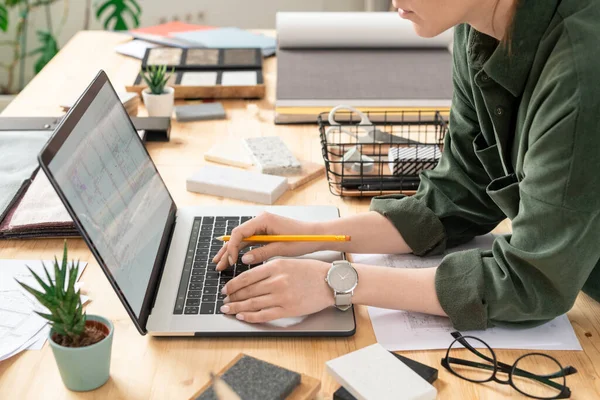 年轻而富有创造力的女设计师一边在笔记本电脑前的桌子上弯腰 一边在工作场所的房子或公寓的电子草图上工作 — 图库照片