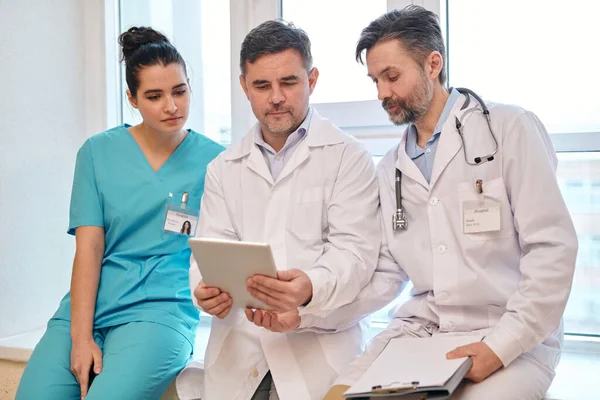 Gruppe Von Fachärzten Sitzt Auf Dem Fensterbrett Und Benutzt Tablet — Stockfoto