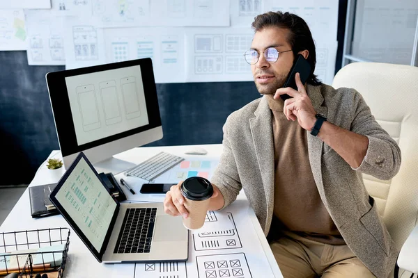 现代自信的男性经理 戴着眼镜坐在桌旁喝咖啡 一边和顾客谈论应用程序的设计 — 图库照片
