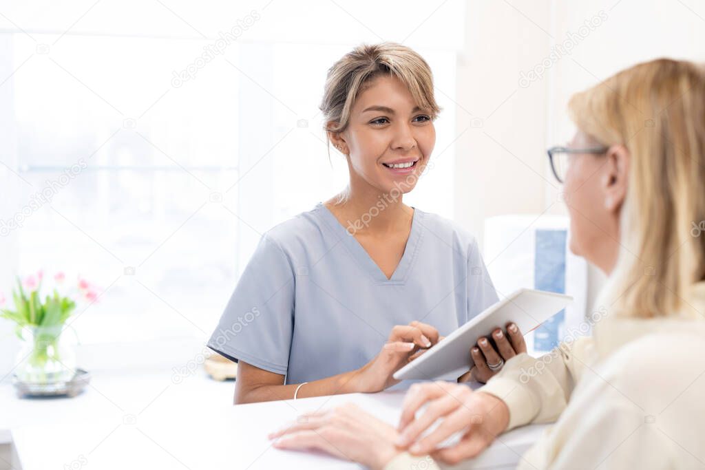 Smiling mixed race beauty salon administrator in scrubs using tablet to check clients appointment