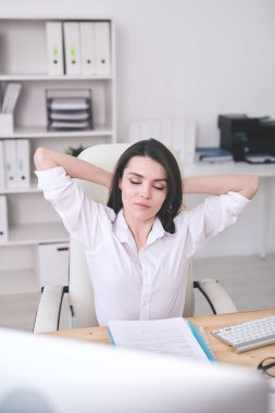 Genç, dingin bayan ofis müdürü ellerini başının arkasında tutarken ve tatilin tadını çıkarırken koltukta dinleniyor.