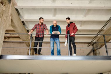 Üç genç mimar daha tamamlanmamış binanın içinde dururken dokunmatik ekranda çizim hakkında konuşuyorlar.