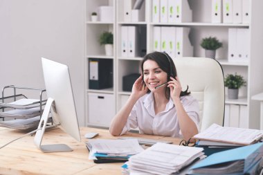 Kulaklıklı, bilgisayar ekranında müşteriye bakan ve soruları cevaplayan mutlu genç müşteri desteği temsilcisi