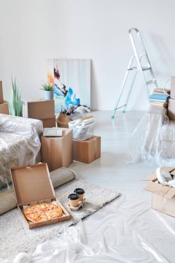 Paketlenmiş kutular ve diğer ıvır zıvırlarla çevrili kanepenin yanında iştah açıcı pizza ve yerde iki bardak kahve olan kutuyu aç.