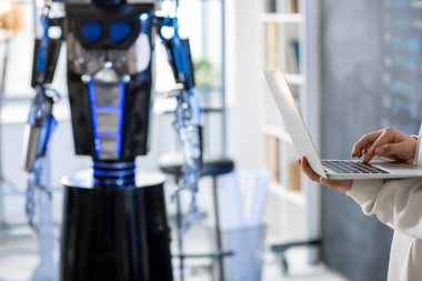 Yeni yazılım geliştiren ya da arka planda robotla teknik proje üzerinde çalışan genç öğrenci ya da programcının eli
