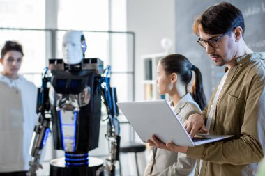 Öğrencileri seminerde robot yeteneklerini sunarken bilgisayarlı ciddi bir öğretmen internetteki materyallere bakıyor.