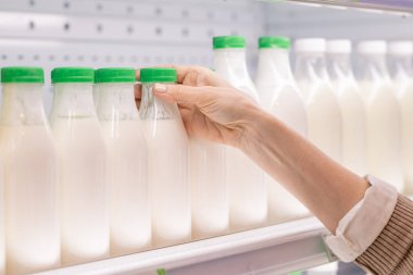 Süpermarkette gıda ürünlerini seçerken bir yandan da plastik şişe taze ekşi süt içen yaşlı kadın tüketiciler.