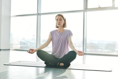 Spor salonundaki ya da spor salonundaki yoga eğitiminde nilüfer pozisyonu alıştırması yaparken paspasın üzerinde oturan dingin, güzel bir kadın.
