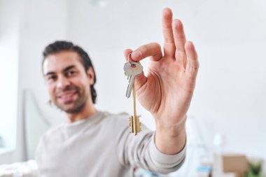 Mutlu genç erkek yerleşimci ya da yeni ev ya da daire alıcısı oturma odasında dururken sana anahtarı gösteriyor.