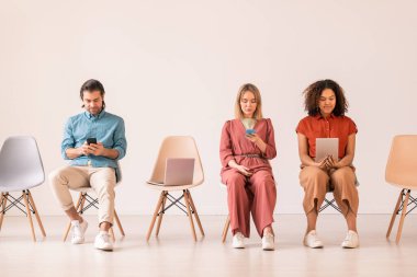 Sosyal medyaya dalmış ciddi çok ırklı genç insanlar sıralanmış sandalyelere oturuyor ve modern aletler kullanıyorlar.