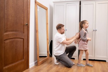 Genç baba, küçük tatlı kızının sırtında küçük bir sırt çantası taşırken okuldan önce eşyalarını toplamasına yardım ediyor.