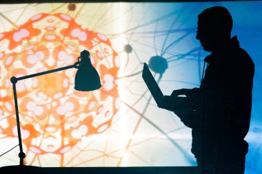 Bilim mühendisinin silueti, parlak projeksiyon ekranına karşı dizüstü bilgisayarda Coronavirus hücresinin 3 boyutlu modelini oluşturuyor.