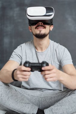 Ev elbiseli sakallı bir adamın VR gözlüklü bir joystick kullanarak sanal video oyunu oynamaktan heyecan duyması.