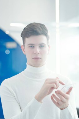 Genç yakışıklı yazılım geliştiricisi ekrandaki düğmeye basıp sana bakarken şeffaf mobil aygıtı işaret ediyor.