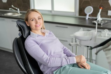 Çağdaş dişçiliğin güzel, genç ve gülümseyen hastası deri koltukta oturmuş klinikte doktorunu bekliyor.