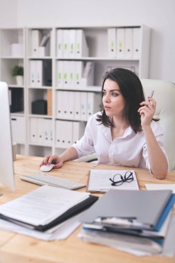 Formalite analisti veya genç kadın muhasebeci ekrandaki çevrimiçi bilgileri incelerken ellerini farenin üzerinde tutuyor.
