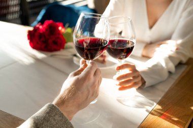 Genç bir adam ve kadının elleri kırmızı şarap kadehleriyle servis edilen masada aşk için kadeh kaldırırken şık bir restoranda.