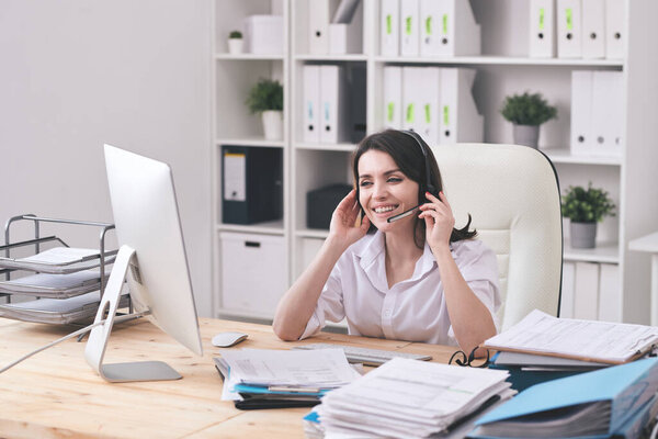 Счастливый молодой представитель службы поддержки клиентов с гарнитурой, смотрящий на клиента на экране компьютера и отвечающий на вопросы
