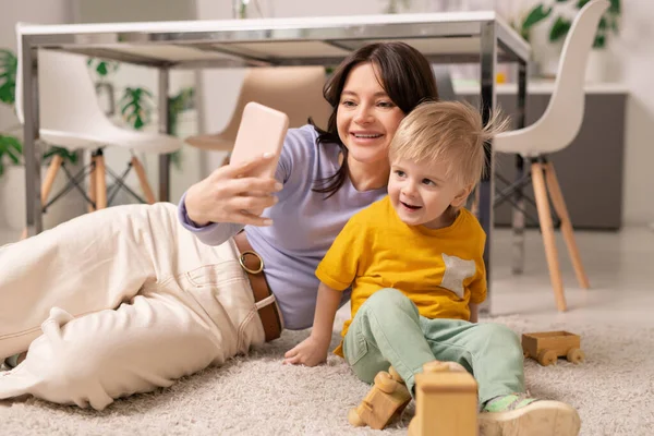 Gelukkig Jong Moeder Leggen Tapijt Met Behulp Van Smartphone Terwijl — Stockfoto