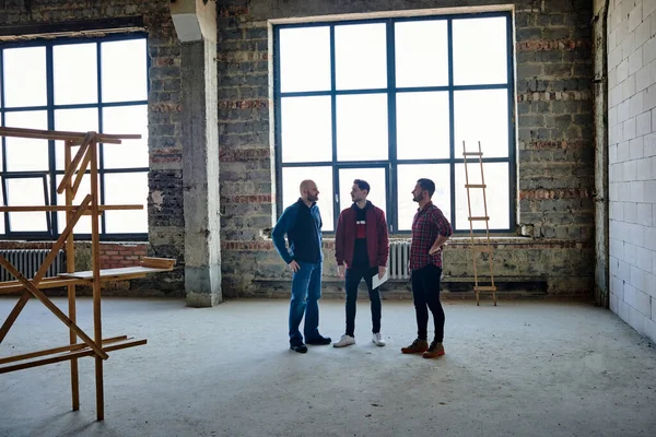 Três Jovens Arquitetos Empreiteiros Contra Janela Centro Grande Sala Inacabada — Fotografia de Stock