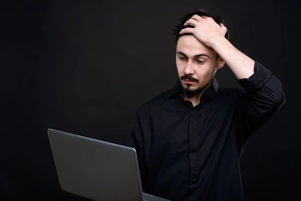 蒙面的年轻程序员头戴黑色衬衫 手牵着手 一边看笔记本电脑屏幕上的信息 — 图库照片