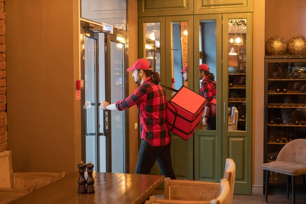 Joven Mensajero Ocupado Con Gran Bolsa Roja Abriendo Puerta Mientras — Foto de Stock