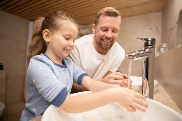 快乐的年轻人一边站在浴室里一边看着他可爱的微笑的小女儿 一边用肥皂洗手 — 图库照片