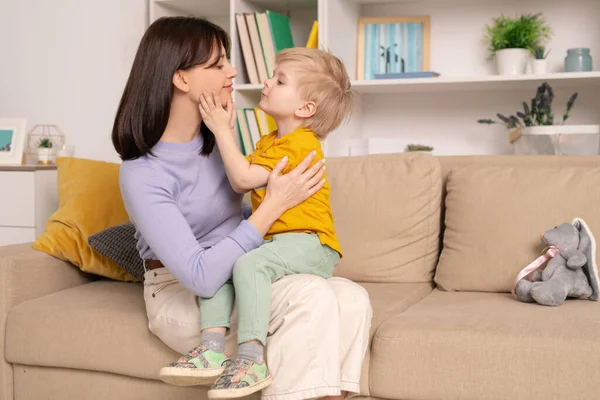 快乐的 充满爱心的年轻妈妈和她可爱的小儿子在家里客厅里坐在柔软的沙发上互诉爱意 — 图库照片