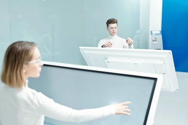 Two young progressive software developers looking through database on large interactive displays while working individually in office