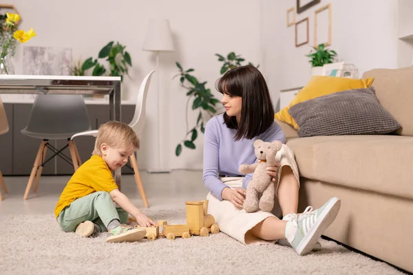 布鲁内特的母亲坐在客厅的地毯上玩玩具 与儿子呆在家里 — 图库照片