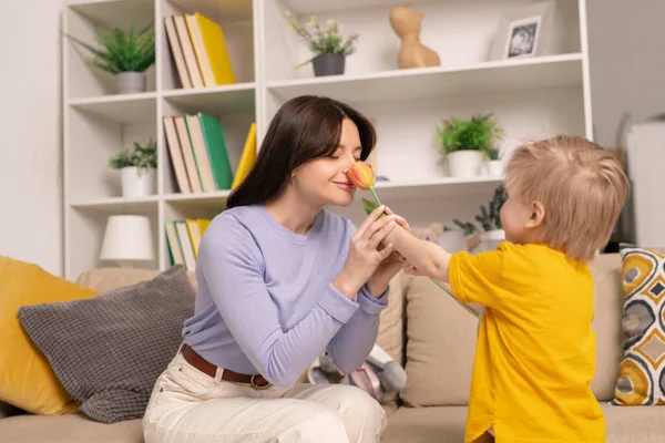 Feliz Madre Joven Atractiva Sentada Sofá Oliendo Flor Dada Por — Foto de Stock