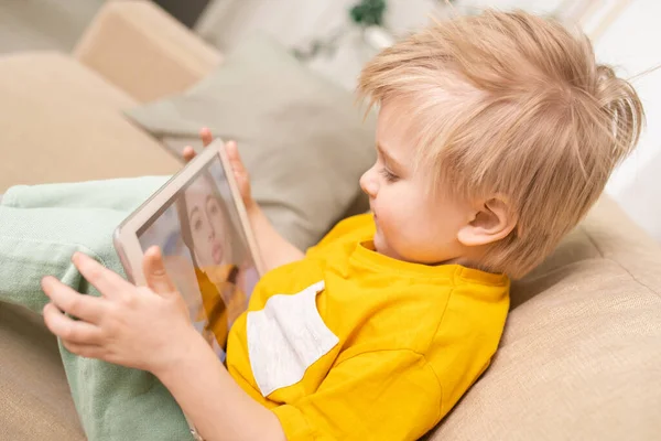 可爱的金发儿子坐在沙发上 一边用平板电脑一边上网一边和妈妈聊天 — 图库照片
