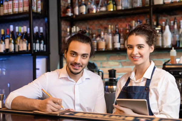 Happy Young Waiter Making Notes Notepad While His Pretty Colleague — Stock Photo, Image