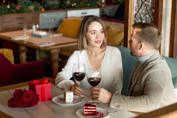 レストランでロマンチックなランチの後にテーブルに座っている間 若い愛情のあるカップルは赤ワインのデザートとガラスで話をしています — ストック写真
