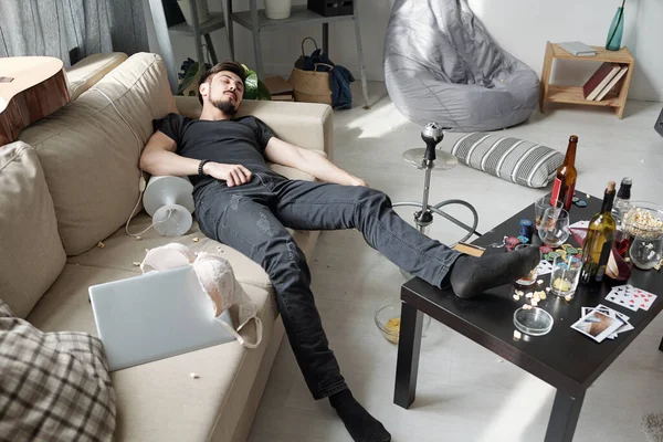 在现代的公寓里 一个疲惫的喝醉了的年轻人睡在沙发上的灯下 — 图库照片