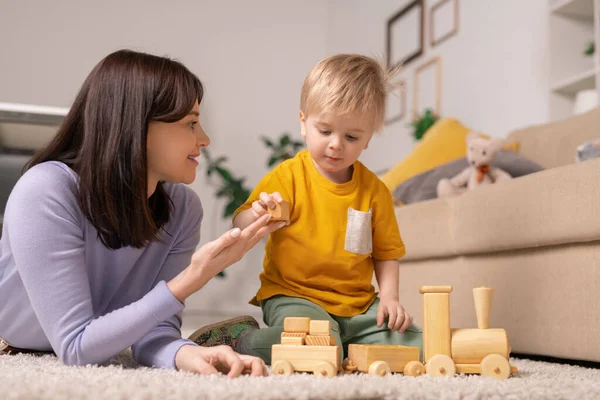 微笑着躺在地毯上的迷人的年轻母亲 把木块送给儿子 同时教他堆积起来的玩具块 — 图库照片