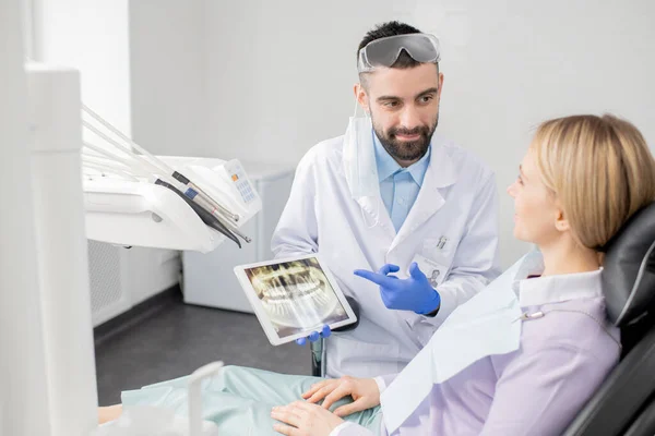 年轻的成功牙医身穿制服 一边用牙齿X光显示触摸屏 一边向他的病人展示该怎么做 — 图库照片