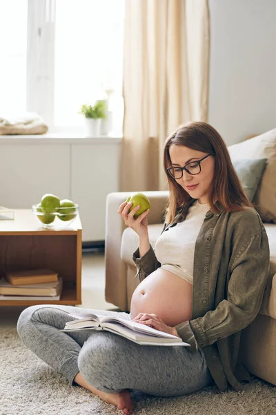 Content Young Pregnant Woman Eyeglasses Sitting Crossed Legs Carpet Eating — Stock Photo, Image