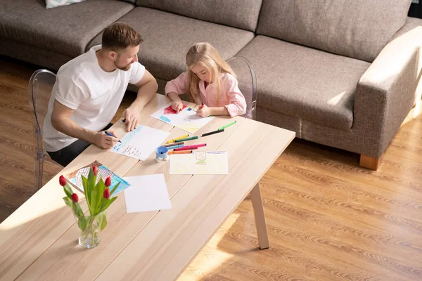 可爱的小女孩用蜡笔或蜡笔在纸上画房子 而她的父亲坐在旁边与她商量 — 图库照片